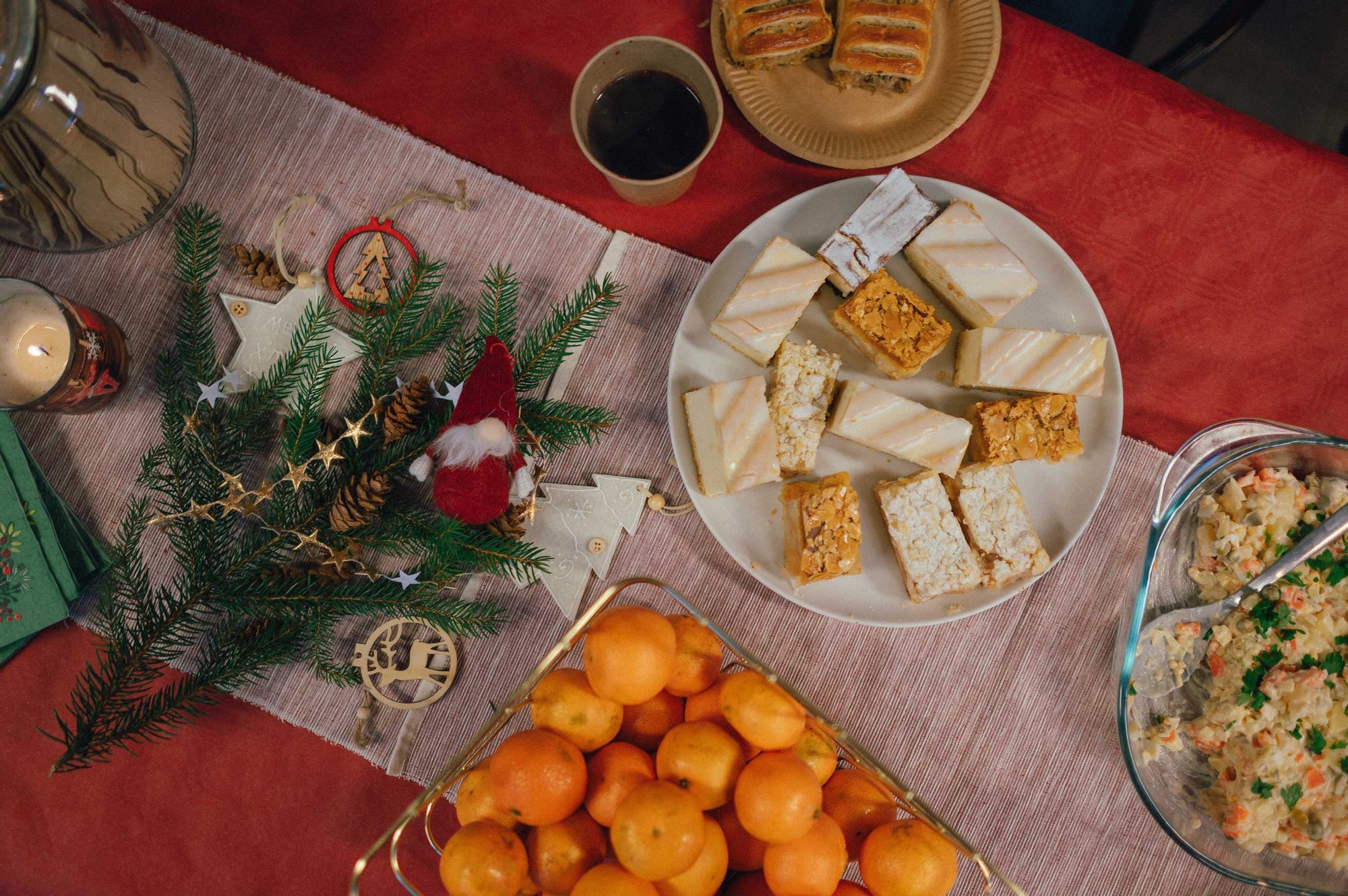 Kolorowa fotografia przedstawia zbliżenie na leżący na stole świąteczny stroik i talerze ze świątecznym potrawami i kubeczek barszczu.