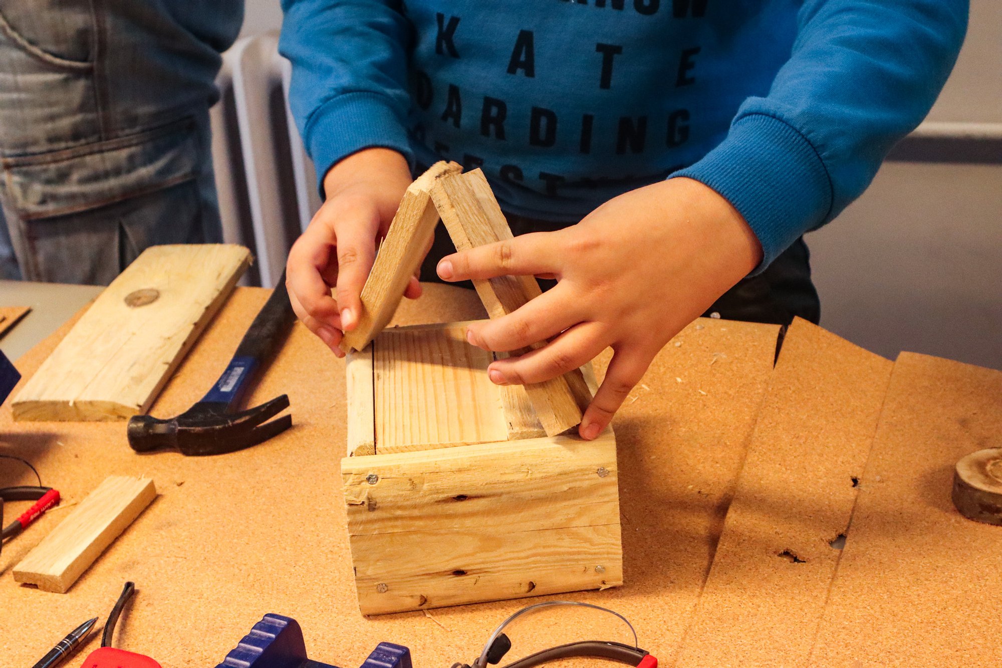 materiały organizatora Zbliżenie na dziecięce dłonie składające zabawkę z drewna. Na stole wokół porozkładane są narzędzia i fragmenty drewna.