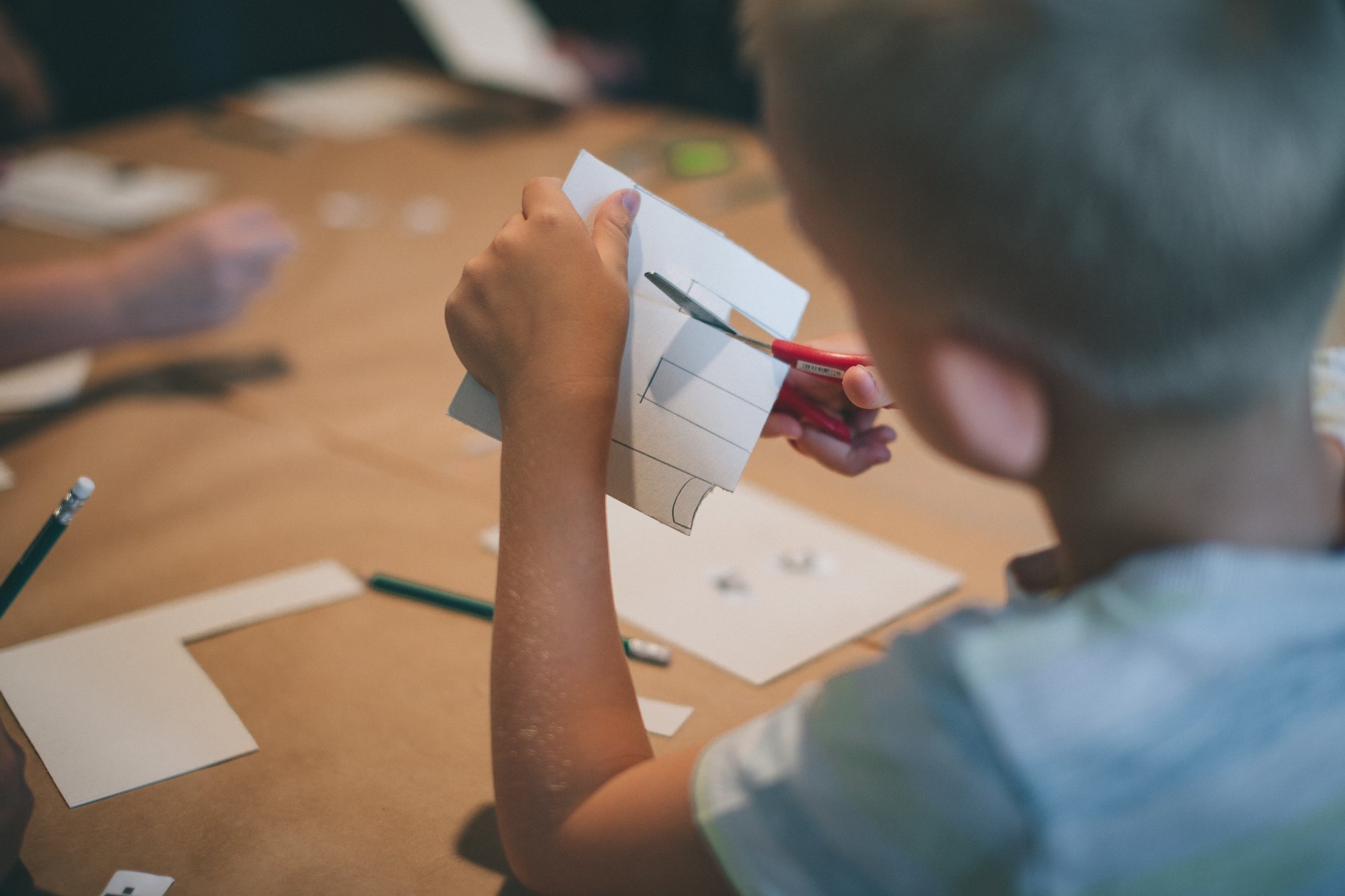 Mały chłopiec wycina kształty z kartki papieru. 