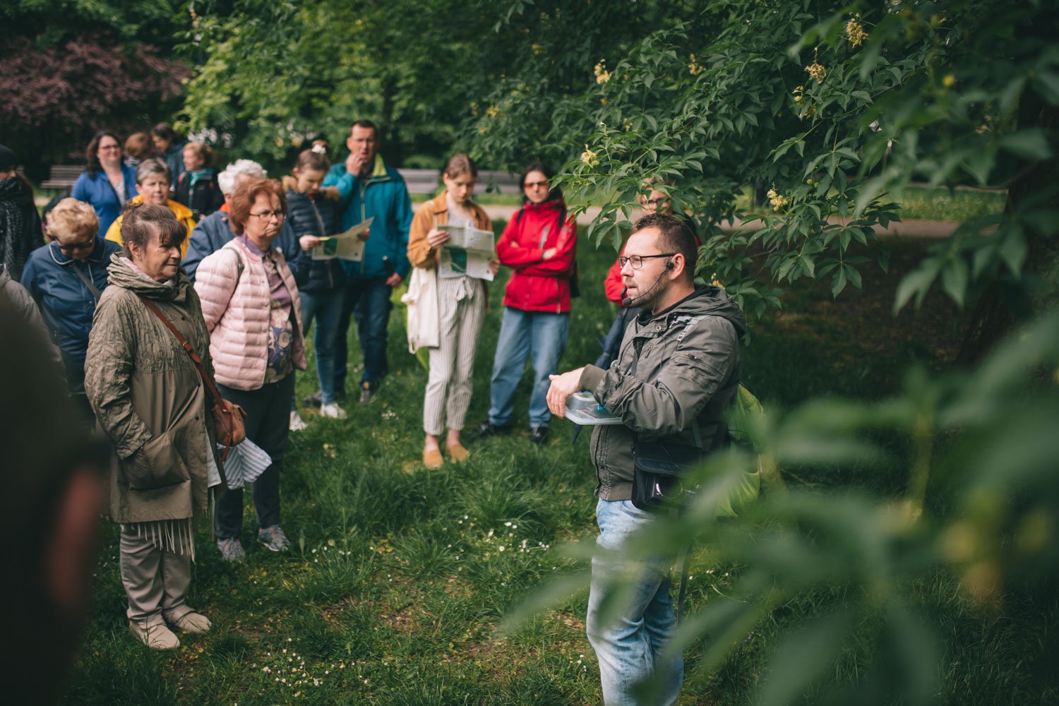 fot. Jerzy Wypych Na trawie pod drzewem stoi grupa ludzi słuchających wykładu młodego mężczyzny.