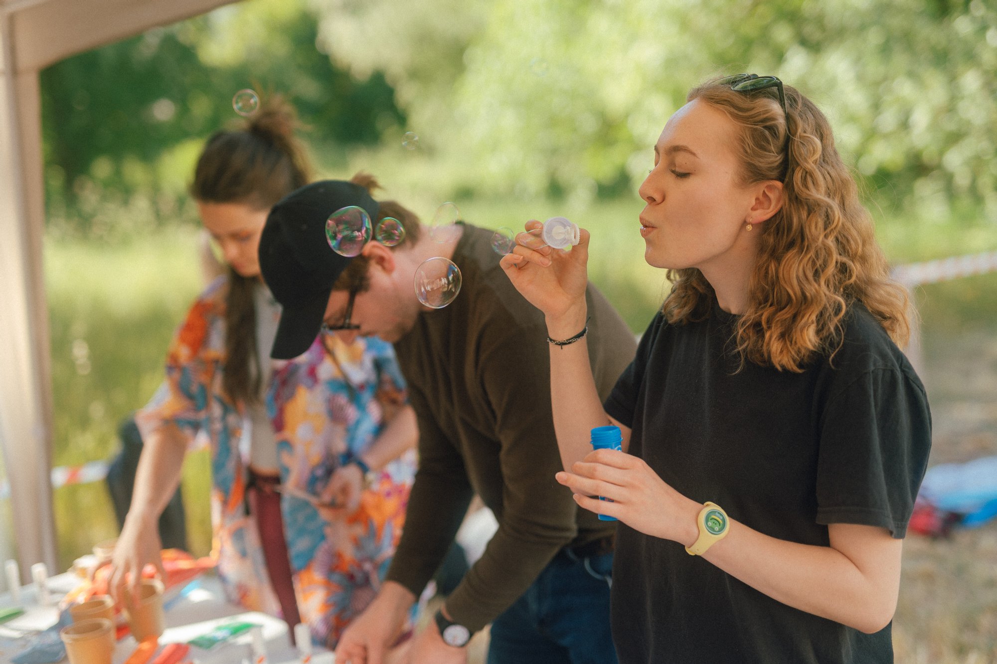 Kolorowa fotografia wykonana podczas sąsiedzkiego pikniku. Młoda kobieta puszcza bańki mydlane.