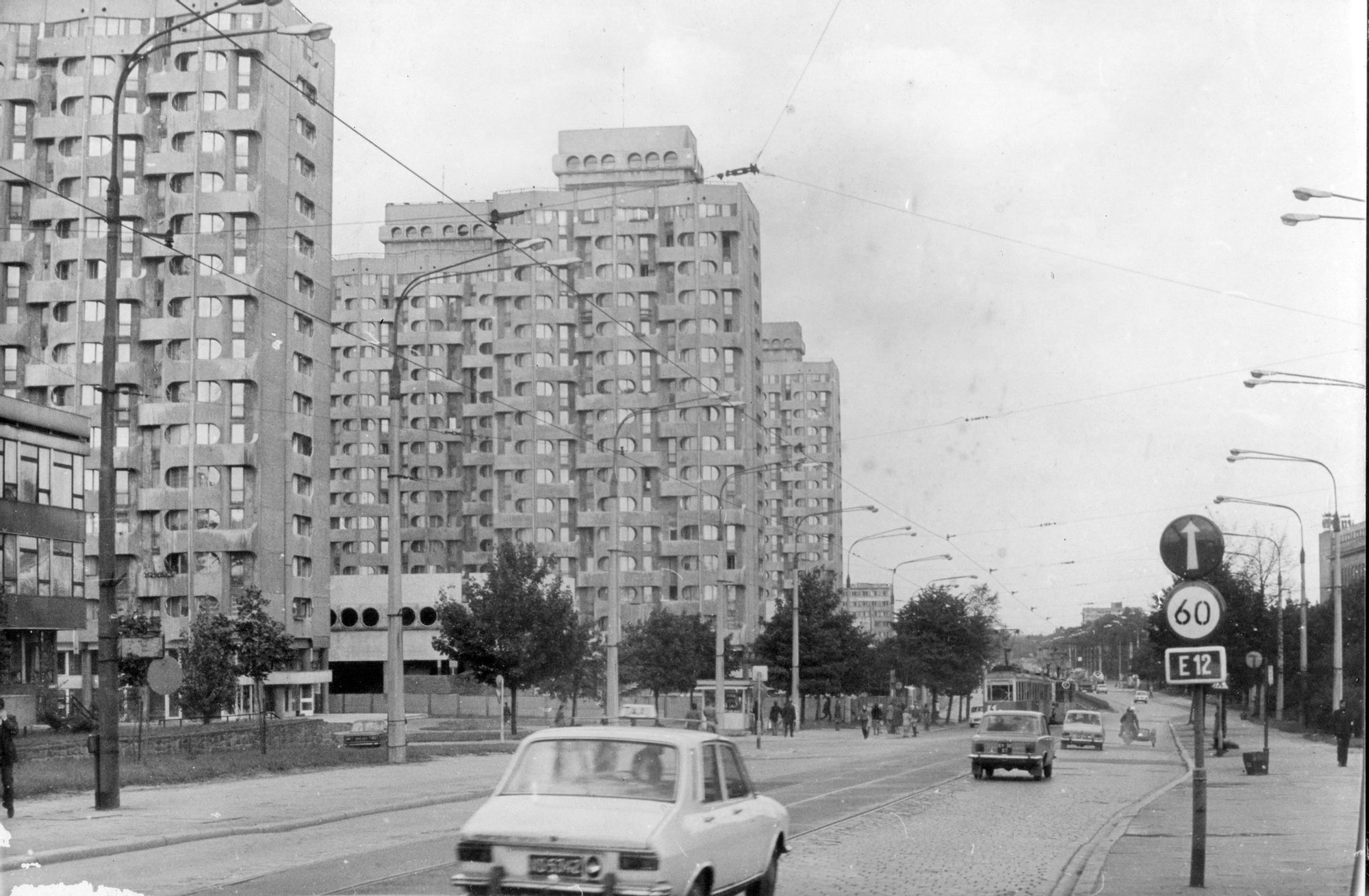 materiały organizatora Archiwalna czarno-biała fotografia. Widok na Plac Grunwaldzki - Manhattan od strony Mostu Grunwaldzkiego. Po lewej stronie wysokie budynki, po prawej stronie ulica z kilkoma przejeżdzającymi samochodami.