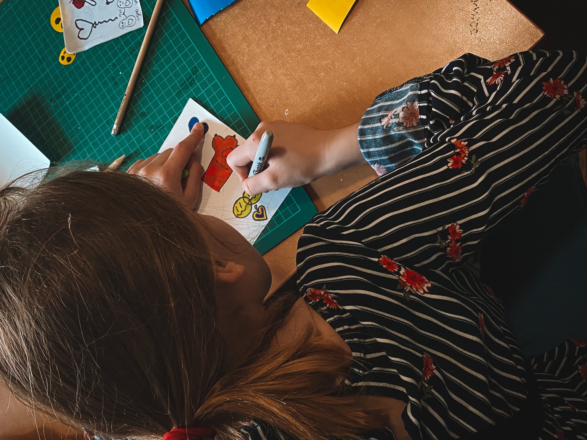 Kilkuletnia dziewczynka pochylona nad biurkiem projektuje naklejki. Kilkuletnia dziewczynka pochylona nad biurkiem projektuje naklejki.