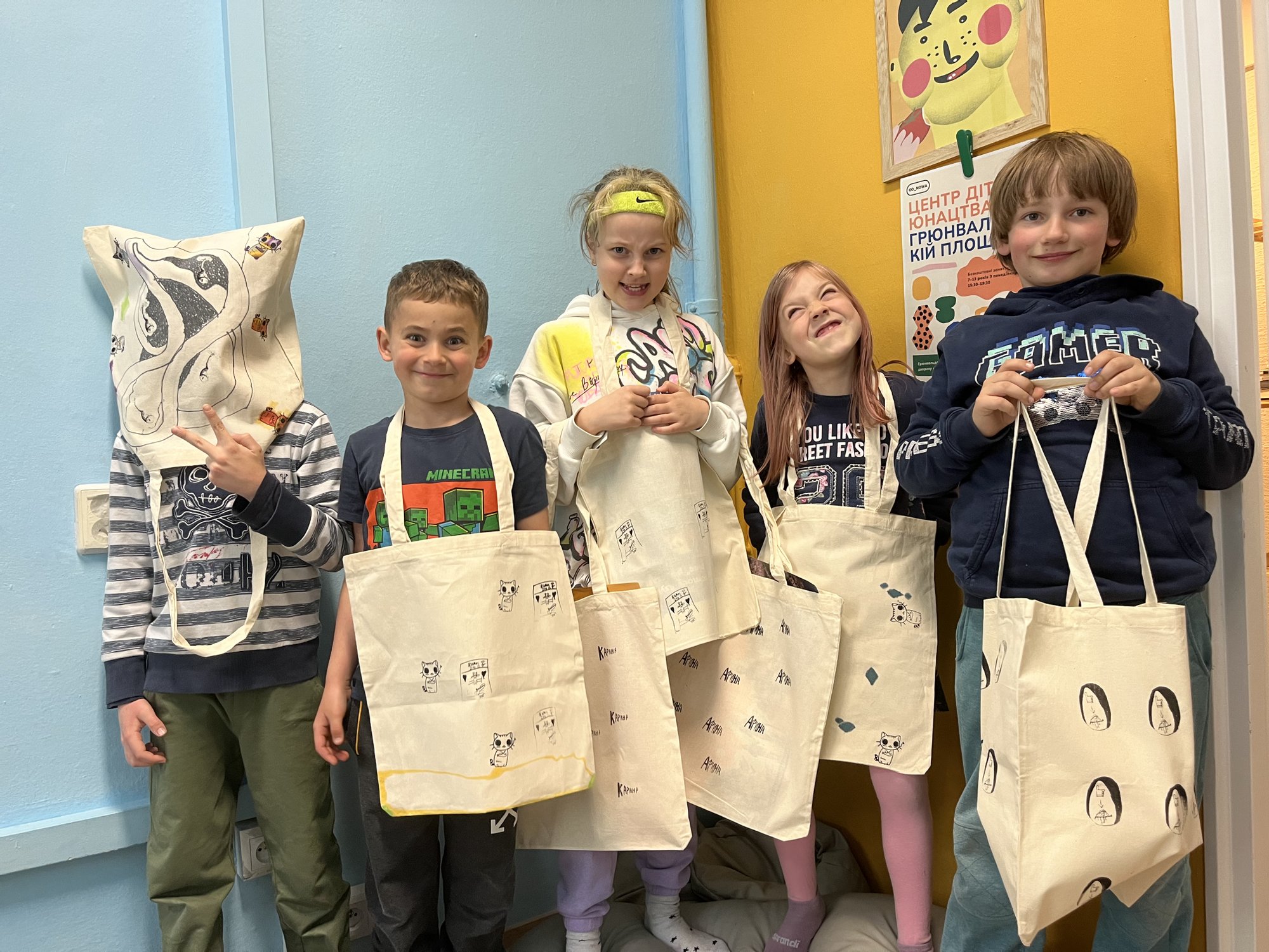 Kolorowa, pozioma fotografia przedstawiająca pięcioro dzieci. Każde ma ze sobą własnoręcznie ozdobioną torbę. Dziecko z lewej strony założyło torbę na głowę. Reszta trzyma torby w rękach.