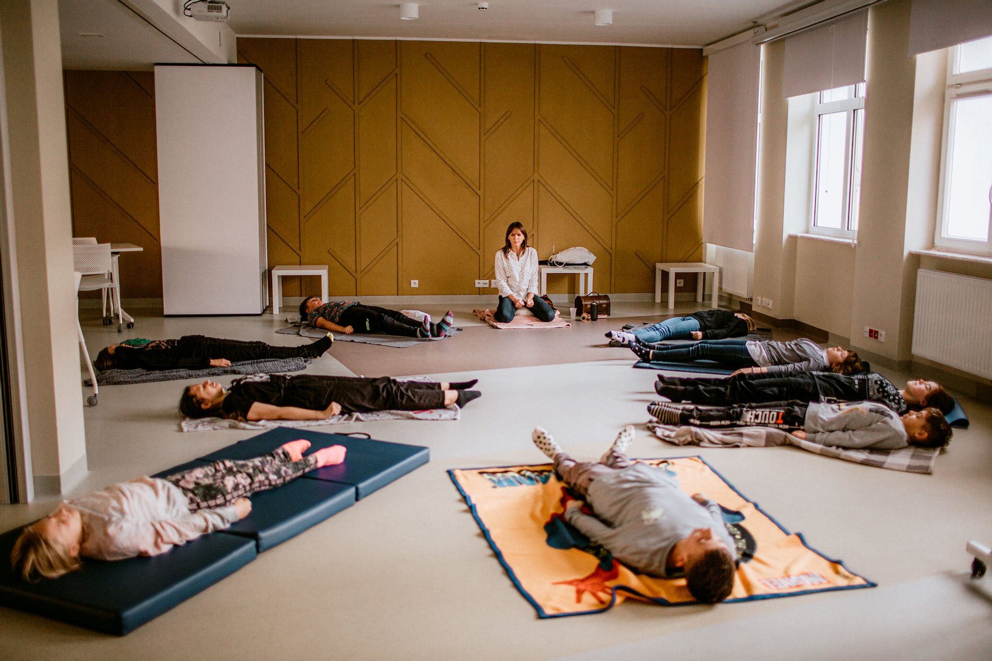 fot. Kalina Żaczek Grupa młodych ludzi siedzi w kręgu na matach w jasnym pomieszczeniu. Trwają warsztaty relaksacyjne.