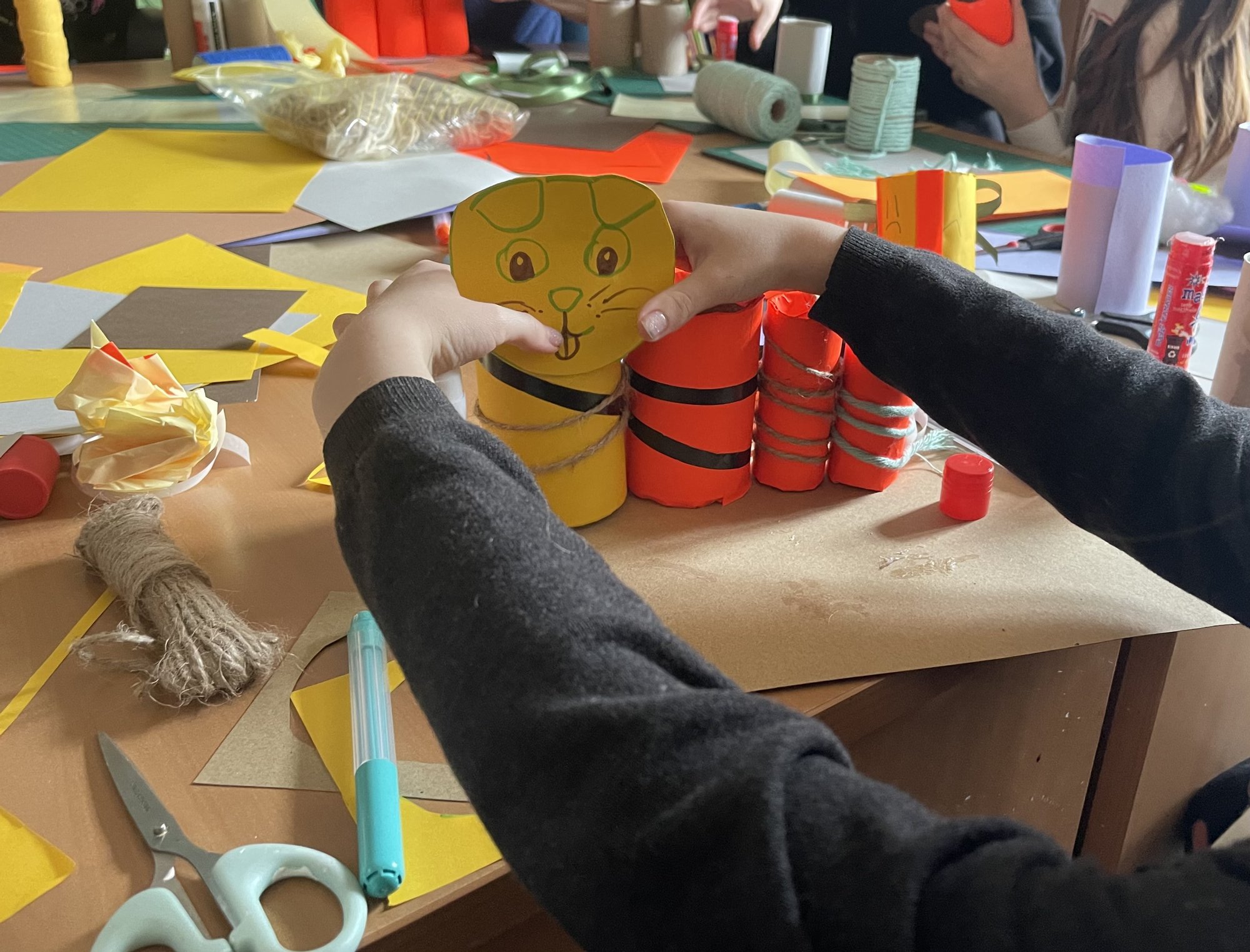 Na dużym stole porozkładane artykuły plastyczne. Zbliżenie na dziecięce dłonie robiące przybornik z papieru. Na dużym stole porozkładane artykuły plastyczne. Zbliżenie na dziecięce dłonie robiące przybornik z papieru.