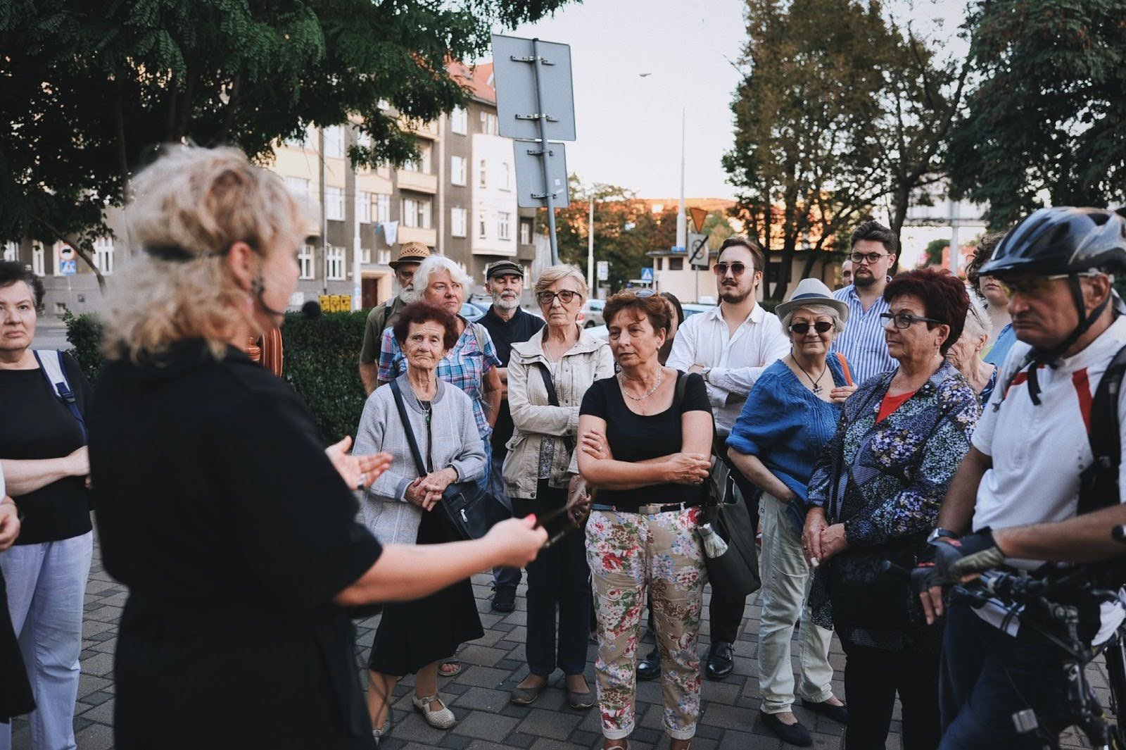 zdjęcie: Anna Pazdej Kolorowa, pozioma fotografia: grupa osób w różnym wieku przystanęła na chodniku, by wysłuchać przewodniczki. Trwa spacer po osiedlu.